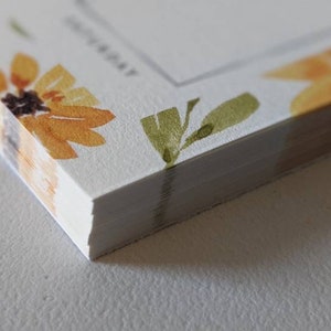May include: A stack of white notepads with a sunflower design border. The notepads have a blank space for writing and the word "TODAY" printed on the top.