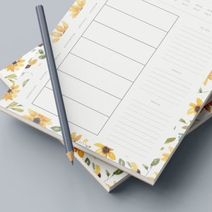 May include: Two stacked floral patterned weekly planners with a pencil on top. The planner has sections for Monday, Tuesday, Wednesday, Thursday, Friday, Saturday, and Sunday. It also has sections for goals, notes, and to do.