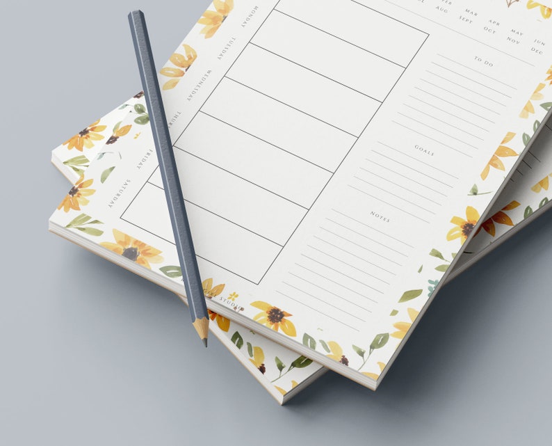 May include: Two stacked floral patterned weekly planners with a pencil on top. The planner has sections for Monday, Tuesday, Wednesday, Thursday, Friday, Saturday, and Sunday. It also has sections for goals, notes, and to do.