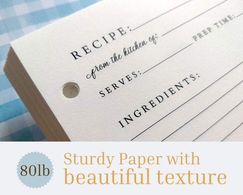 May include: A stack of white recipe cards with a hole punched in the top corner. The cards have lines for writing down a recipe, including the name, ingredients, servings, and prep time. The text "RECIPE: from the kitchen of:" is printed on the card. The cards are made of sturdy paper with a beautiful texture. The text "80lb" is printed on a blue circle.