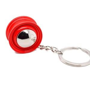 May include: A red metal keychain shaped like a car wheel with a silver center. The keychain has a silver chain and a silver ring.