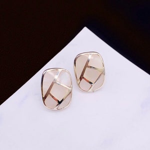 May include: A pair of silver earrings with white mother-of-pearl inlays. The earrings are rectangular in shape and have a geometric design.