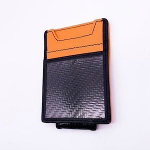 May include: A black and orange leather wallet with a money clip. The wallet has a carbon fiber pattern on the front.