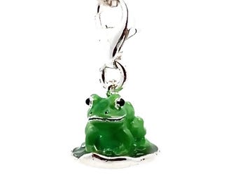 May include: A silver charm necklace with a green frog charm. The frog is sitting on a lily pad and has black eyes.