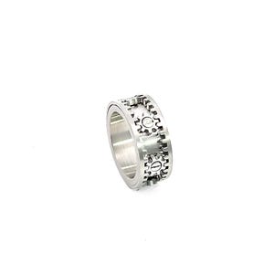 May include: A silver-colored ring featuring a gear design. The ring has a band with repeating gear patterns around the circumference. The gears are detailed with visible teeth and circular centers, creating a mechanical aesthetic.