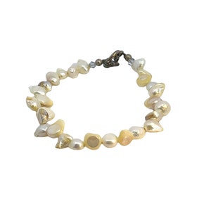 May include: A delicate bracelet made of natural pearls in shades of white and cream. The pearls are strung together with a silver clasp.