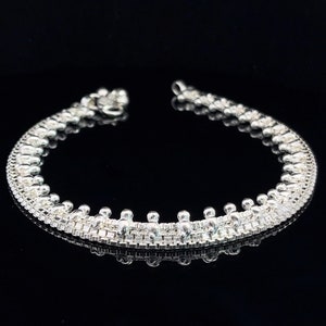 May include: A silver anklet with a delicate chain design and small round beads. The anklet is made of a woven chain with a row of beads along the bottom edge.