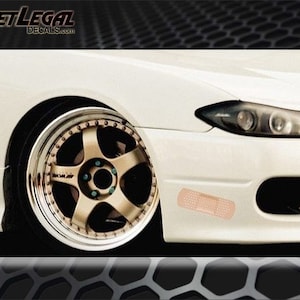 May include: A white car with a gold rim and a bandage sticker on the front bumper.