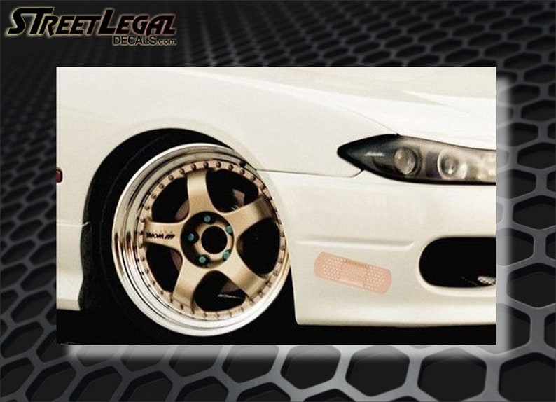 May include: A white car with a gold rim and a bandage sticker on the front bumper.