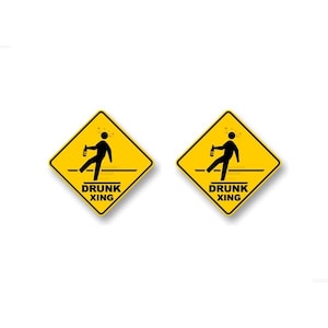 May include: Two yellow diamond-shaped warning signs with black borders. Each sign depicts a stick figure with a bottle in one hand, stumbling and falling. The text on each sign reads "DRUNK XING".