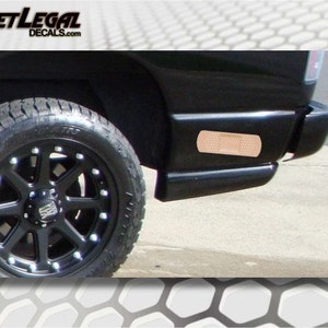 May include: A black pickup truck with a black wheel and a brown band-aid sticker on the rear bumper. The truck is parked on a gray concrete surface.