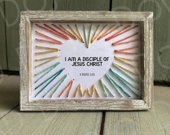 Puede incluir: Una pieza de bordado enmarcada con un fondo blanco y puntadas de hilo de colores en forma de corazón. El texto "I AM A DISCIPLE OF JESUS CHRIST" está centrado en el corazón. La referencia bíblica "3 NEPHI 5:13" está debajo del texto.