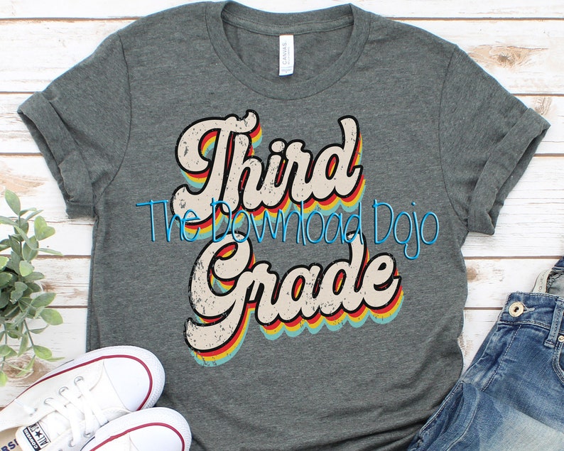 May include: A gray t-shirt with the words "Third Grade" in a retro font with rainbow accents. The text "The Download Dojo" is in a blue script font. The shirt is paired with white sneakers and blue jeans.