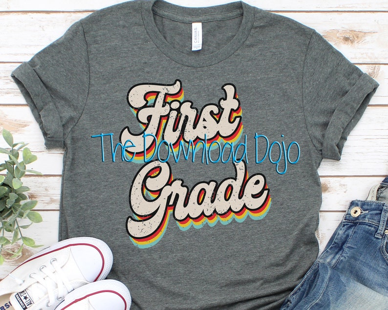 May include: A gray t-shirt with a retro-style graphic that says "First Grade" in rainbow colors. The graphic has a distressed look and is centered on the shirt.