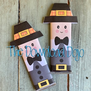 May include: Two paper craft figures resembling pilgrims, each with a black hat, a bow tie, and a gray suit. The figures have smiling faces with rosy cheeks. The text "The Download Dojo" is written in blue cursive across the image.