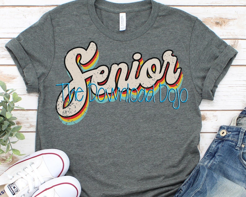 Puede incluir: Una camiseta gris oscuro con un gr&aacute;fico de estilo retro que dice "Senior" en colores arco&iacute;ris. El gr&aacute;fico tiene un aspecto desgastado y est&aacute; rodeado por un contorno blanco.