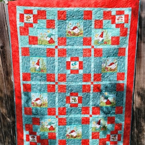 May include: A red and teal quilt with a patchwork design featuring gnomes and mushrooms. The quilt is made with a variety of fabrics and has a quilted texture.