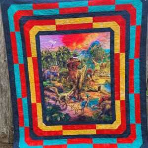 May include: A colorful quilt with a dinosaur theme. The quilt features a large dinosaur in the center surrounded by other dinosaurs and plants. The quilt is framed with a multi-colored border.