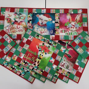 May include: Set of six Christmas-themed quilted placemats and coasters featuring various animal designs with holiday greetings. The placemats are red and green with a checkered pattern and the coasters are smaller versions of the placemats.
