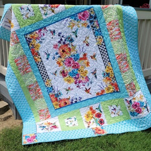 May include: A colorful quilt with a floral and bird design. The quilt is made with a variety of fabrics, including blue, green, and white. The quilt is quilted with a pattern of circles.