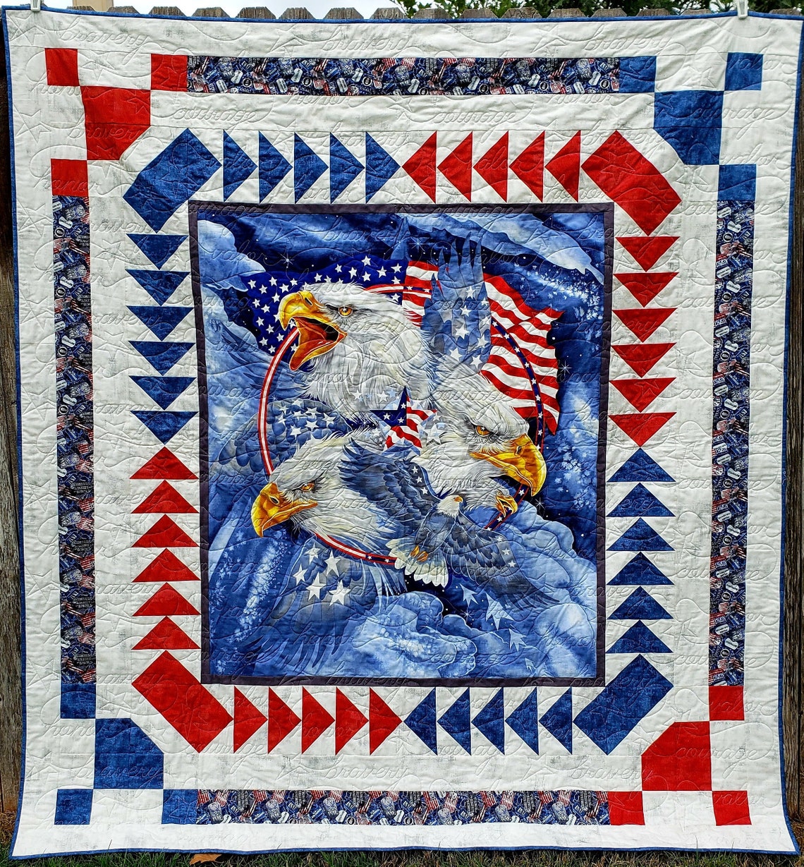 May include: Patriotic quilt featuring a vibrant blue, red, and white color scheme. The central design showcases four majestic bald eagles against a backdrop of American flags. The quilt's border is adorned with a geometric pattern of red and blue triangles on a white background. This handcrafted quilt is perfect for adding a touch of Americana to any home decor.