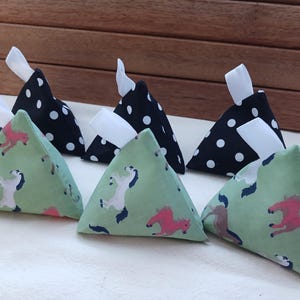 May include: Six triangular fabric sachets. Three are black with white polka dots, and three are light green with a horse pattern in pink, white, and blue. Each sachet has a white ribbon attached.
