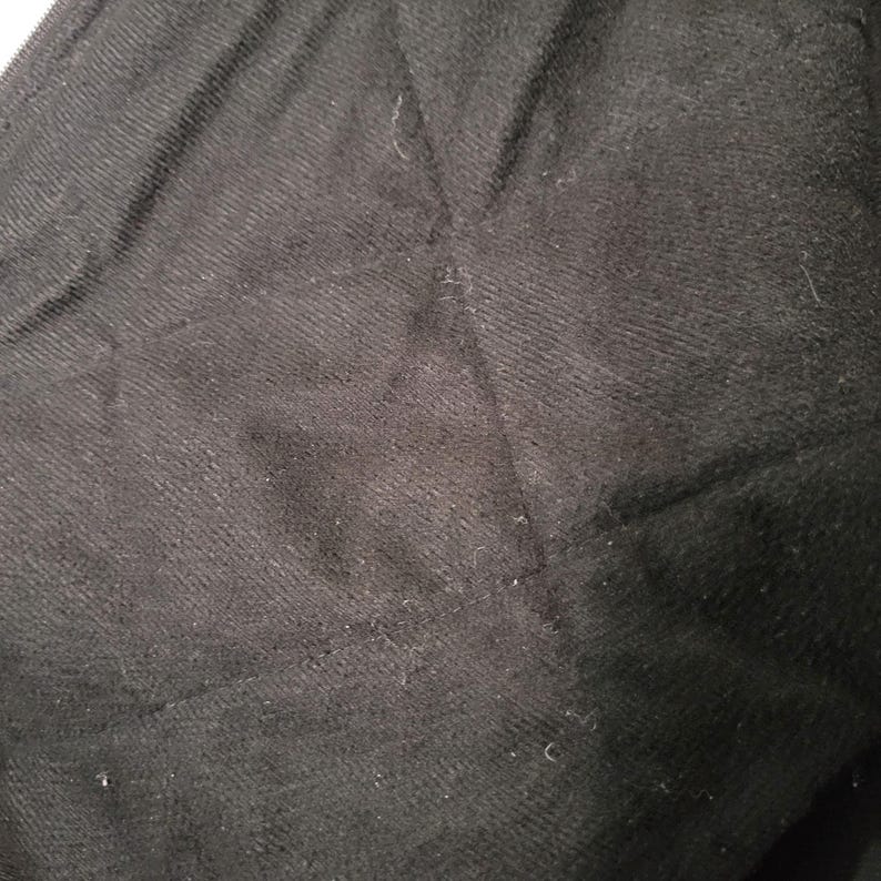 May include: Close-up of a black fabric with a textured surface. The fabric appears to be a dark, solid color, possibly a knit or woven material. The image shows the details of the fabric's texture and weave.