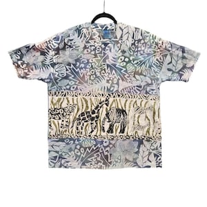 May include: Short-sleeved shirt with a pattern of leaves, animal prints, and geometric shapes. The bottom panel features a giraffe, elephant, and other animals. The shirt is hanging on a black hanger.