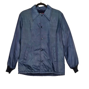 May include: A navy blue jacket with a button-up front, two front pockets, and a collar. The jacket has long sleeves with black cuffs. The jacket is hanging on a black hanger against a white background.