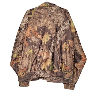 May include: A camouflage jacket with a brown, green, and tan leaf pattern. The jacket has a collared neckline, a zipper closure, and elastic cuffs and waistband. The jacket is hanging on a hanger.