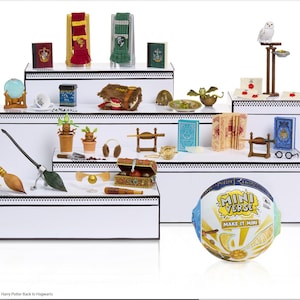 May include: A display of miniature Harry Potter-themed collectibles, including books, brooms, and a golden snitch. The items are arranged on tiered white platforms. A Mini Verse ball is in the foreground.
