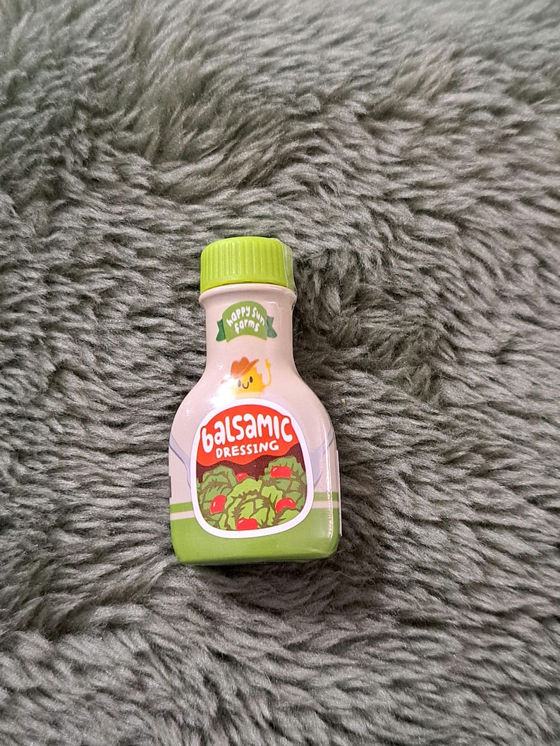 May include: A green plastic bottle with a green cap and a label that says "Happy Sun Farms Balsamic Dressing". The label has a cartoon sun with a smiling face and a green leaf.