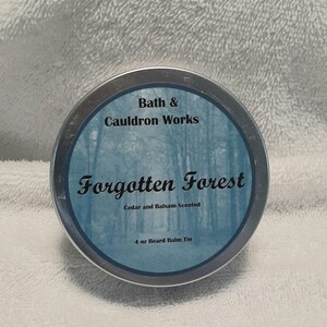 May include: A silver tin with a blue label that reads "Bath & Cauldron Works Forgotten Forest Cedar and Balsam Scented 4 oz Beard Balm Tin".