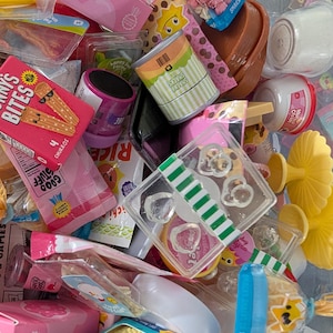 Puede incluir: Una colección de alimentos en miniatura, que incluye cajas de churros, pasta y snacks. Los artículos son de varios colores, como rosa, verde y amarillo. Algunos paquetes tienen texto como "Happy Farm" y "Good Stuff".