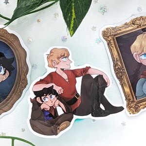 May include: Three illustrated stickers featuring portraits of characters in ornate gold frames. The first sticker shows a young man with dark hair and blue eyes in a red scarf. The second sticker shows two young men, one with blonde hair and the other with dark hair, sitting together. The third sticker shows a young man with blonde hair and blue eyes wearing a red scarf and silver armor.