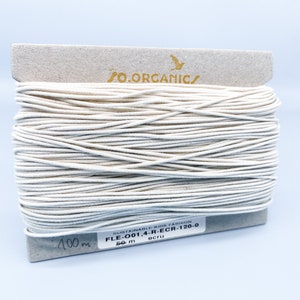 May include: A spool of 50 meters of ecru-colored elastic cord, labeled "O.ORGANIC/ SUSTAINABLE KIDS FASHION FLE-001,4-R-ECR-120-0 ecru 50 m".