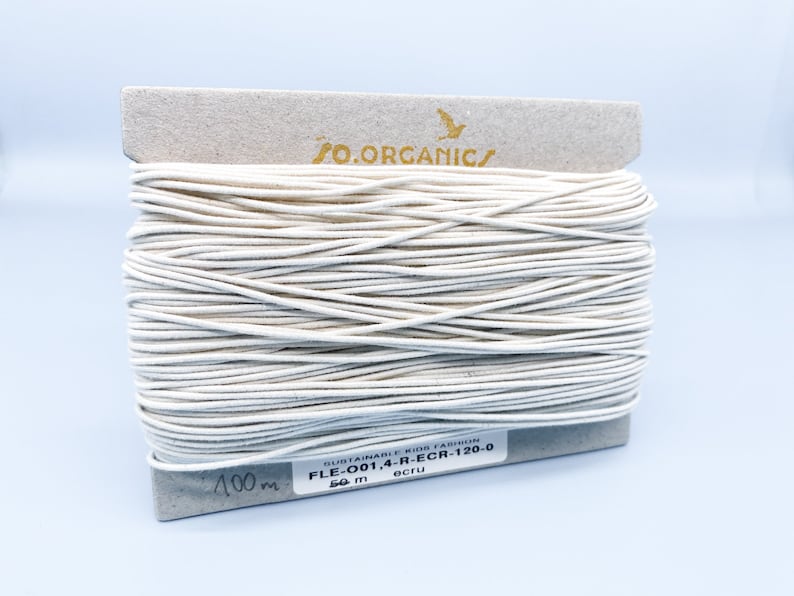 May include: A spool of 50 meters of ecru-colored elastic cord, labeled "O.ORGANIC/ SUSTAINABLE KIDS FASHION FLE-001,4-R-ECR-120-0 ecru 50 m".