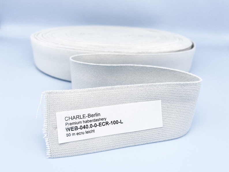 May include: A roll of white elastic band with a label that reads "CHARLE-Berlin Premium haberdashery WEB-040.0-0-ECR-100-L 50 m ecru leicht"