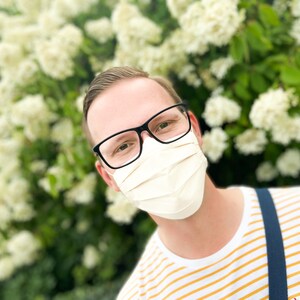 May include: A person wearing a white face mask and black framed glasses. The person is wearing a yellow and white striped shirt with a blue strap.