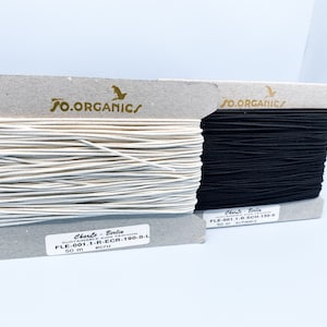 May include: Two spools of elastic cord, one white and one black, with labels that read "SO.ORGANIC/" and "Charte Berlin" with product codes and color names. Each spool contains 50 meters of elastic cord.