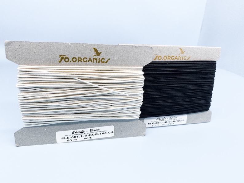 May include: Two spools of elastic cord, one white and one black, with labels that read "SO.ORGANIC/" and "Charte Berlin" with product codes and color names. Each spool contains 50 meters of elastic cord.
