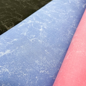 Könnte beinhalten: Nahaufnahme von drei Stoffmustern. Die Muster sind aufgerollt und zeigen eine dunkelgraue, hellblaue und rosafarbene Farbe. Der Stoff hat eine strukturierte, abgenutzte Optik.