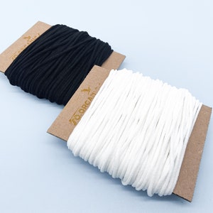 May include: Two spools of elastic cord, one black and one white, on brown cardboard spools with the text "70 ORGANIX" printed on the white spool.
