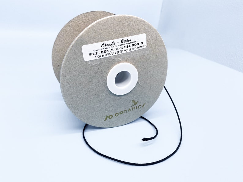 May include: A spool of black 100 meter passepoil trim, a type of fabric trim, on a cardboard spool with a white label that reads "CharLe-Berlia SUSTAINABLE KIDS FASHION FLE-001.5-R-SCH-000-0 100mPASSEPOIL.schwar" and a green logo that reads "FO.ORGANICS".