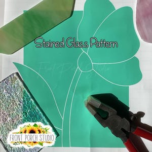 以下が含まれることがあります： 「Stained Glass Pattern」の文字と花の輪郭が描かれた、ターコイズ色のステンドグラスパターン。様々な色のガラス片がパターン周辺に散らばっており、赤と黒のペンチも写っています。画像には「Front Porch Studio」のロゴも含まれています。