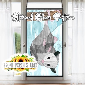May include: Stained glass pattern of a possum hanging upside down. The possum is gray with pink ears and a white face. The background is a light blue watercolor wash.