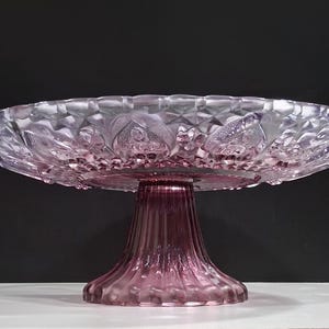 Pu&ograve; includere: Un'alzatina per torte vintage nei toni del rosa e del viola. L'alzatina in vetro presenta un design dettagliato e strutturato sulla ciotola e sulla base. La ciotola ha un motivo a diamante e accenti floreali. La base ha un design scanalato.