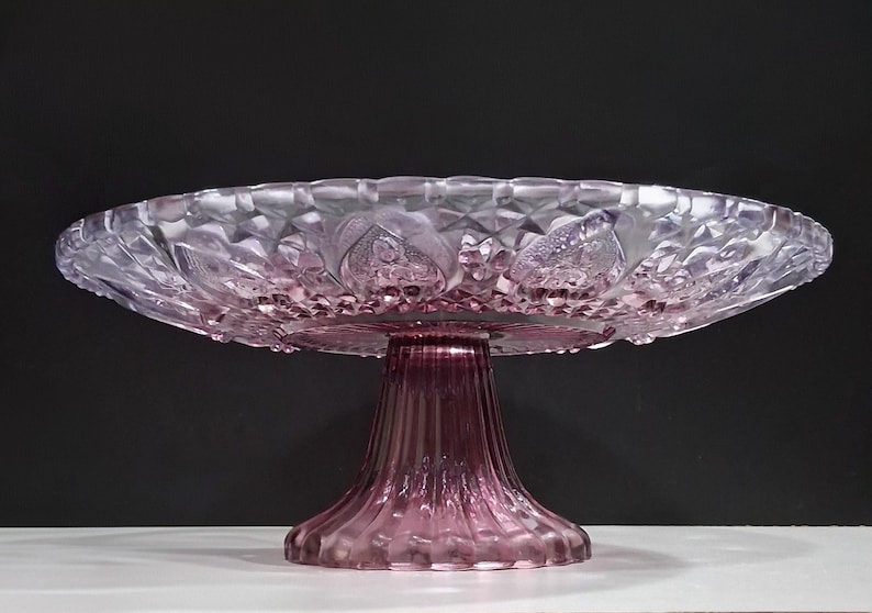 Pu&ograve; includere: Un'alzatina per torte vintage nei toni del rosa e del viola. L'alzatina in vetro presenta un design dettagliato e strutturato sulla ciotola e sulla base. La ciotola ha un motivo a diamante e accenti floreali. La base ha un design scanalato.