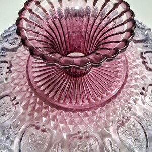 Pu&ograve; includere: Un'alzatina per torte in vetro vintage con un design bicolore. La base &egrave; viola chiaro con dettagli a forma di cuore, mentre la parte superiore e il centro sono di un viola pi&ugrave; scuro. L'alzatina ha un bordo smerlato.