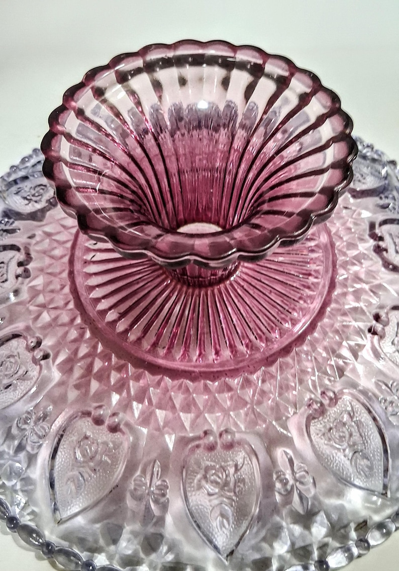 Pu&ograve; includere: Un'alzatina per torte in vetro vintage con un design bicolore. La base &egrave; viola chiaro con dettagli a forma di cuore, mentre la parte superiore e il centro sono di un viola pi&ugrave; scuro. L'alzatina ha un bordo smerlato.
